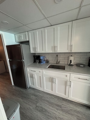 Una cocina moderna con armarios blancos, un refrigerador de acero inoxidable, un fregadero y una cafetera.