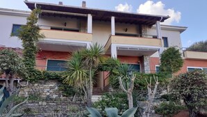 Un edificio de varios pisos con balcones, una pared de piedra y diversas plantas.