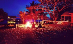 A beach scene with a fire, palm trees, and a building with steps leading to a door.