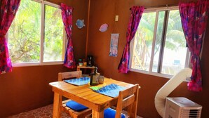Ein Zimmer mit einem Holztisch, blauen Kissen, einem Ventilator und einem Fenster mit Vorhängen.