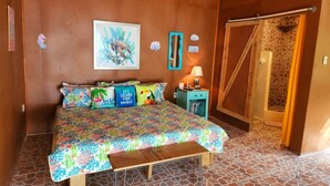Ein Schlafzimmer mit Bett, einer Bank, einem Nachttisch, einem Spiegel und einer Tür zu einem Badezimmer.