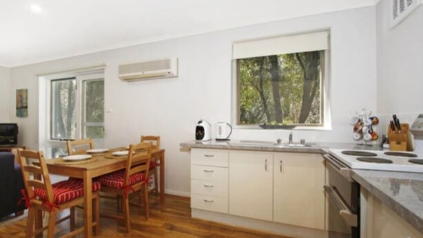 Una cocina moderna con armarios de madera, una mesa de comedor con sillas y un ventanal con vistas a árboles.
