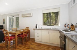 A modern kitchen with wooden cabinets, a dining table with chairs, and a window with a view of trees.