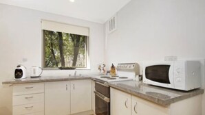 Una cocina moderna con armarios blancos, horno empotrado, microondas y ventana con vistas a árboles.