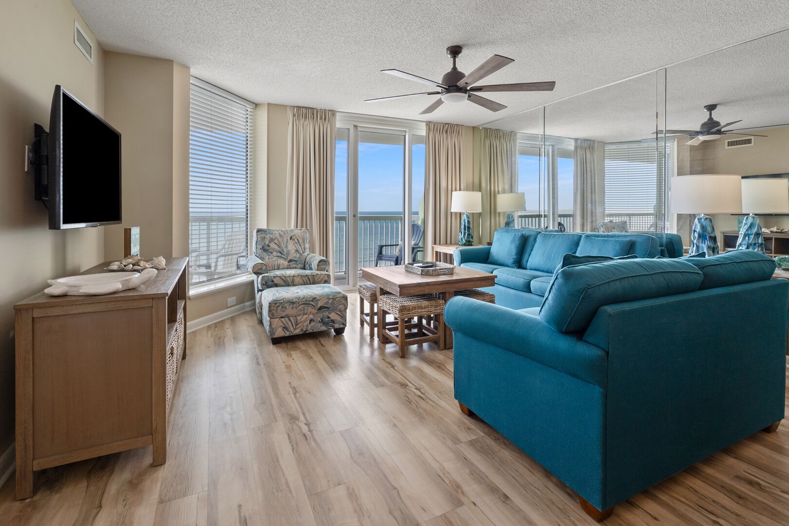 A spacious living room with a large blue sofa, a wooden coffee table, and a television mounted on the wall.
