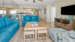 Un salon spacieux avec une table basse en bois, des canapés bleus, un téléviseur et une pancarte sur laquelle on peut lire : « Bienvenue dans notre maison de vacances en bord de mer ».