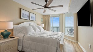 Une chambre à coucher avec un lit, une table de chevet, une lampe, un ventilateur de plafond et un téléviseur.