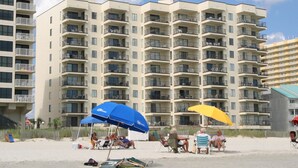 A beachfront hotel with multiple balconies, beach chairs, and umbrellas.