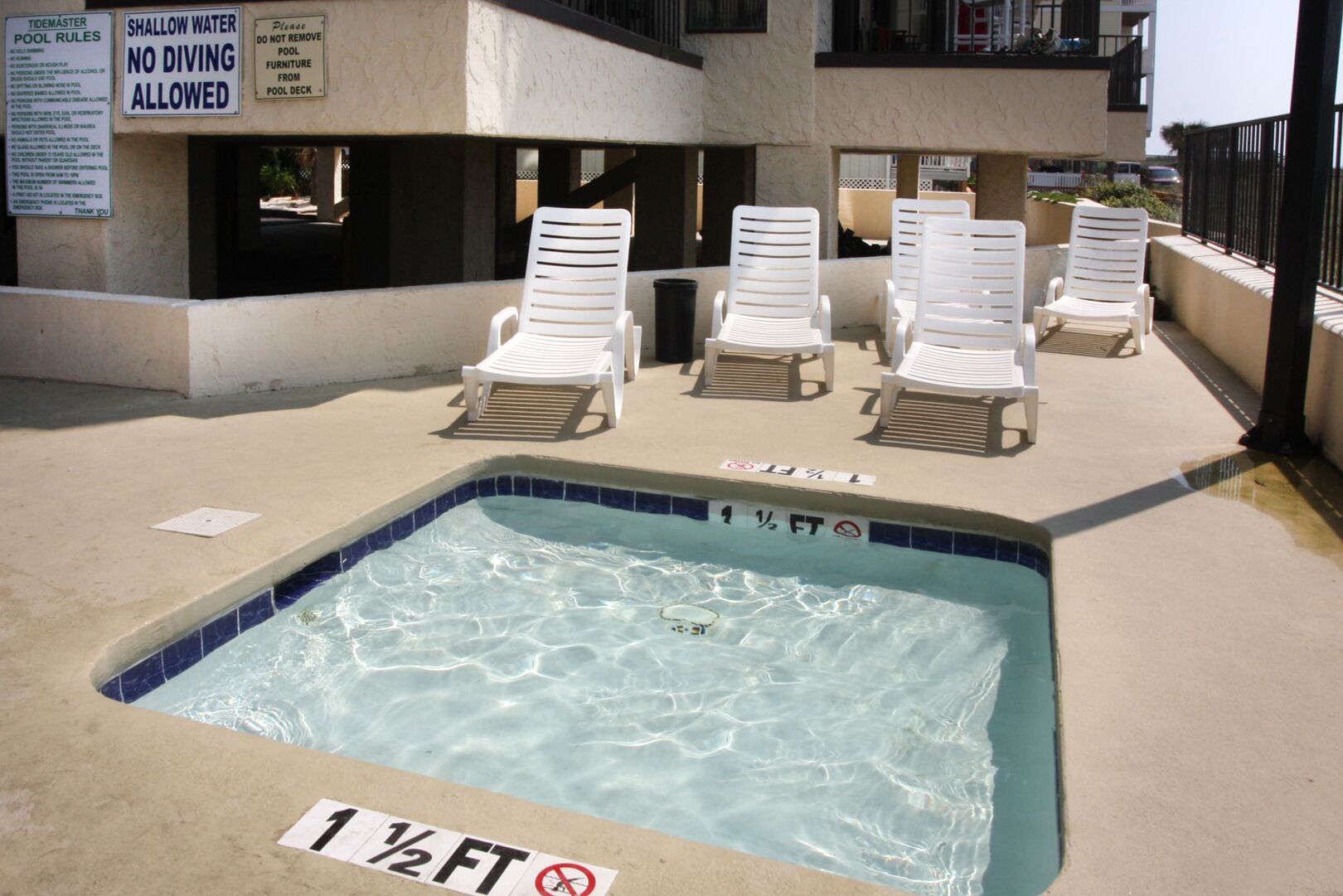 A shallow water pool with lounge chairs and a sign indicating no diving allowed.