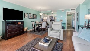 A living room with a TV, a sofa, a coffee table, and a dining area with chairs and a table.