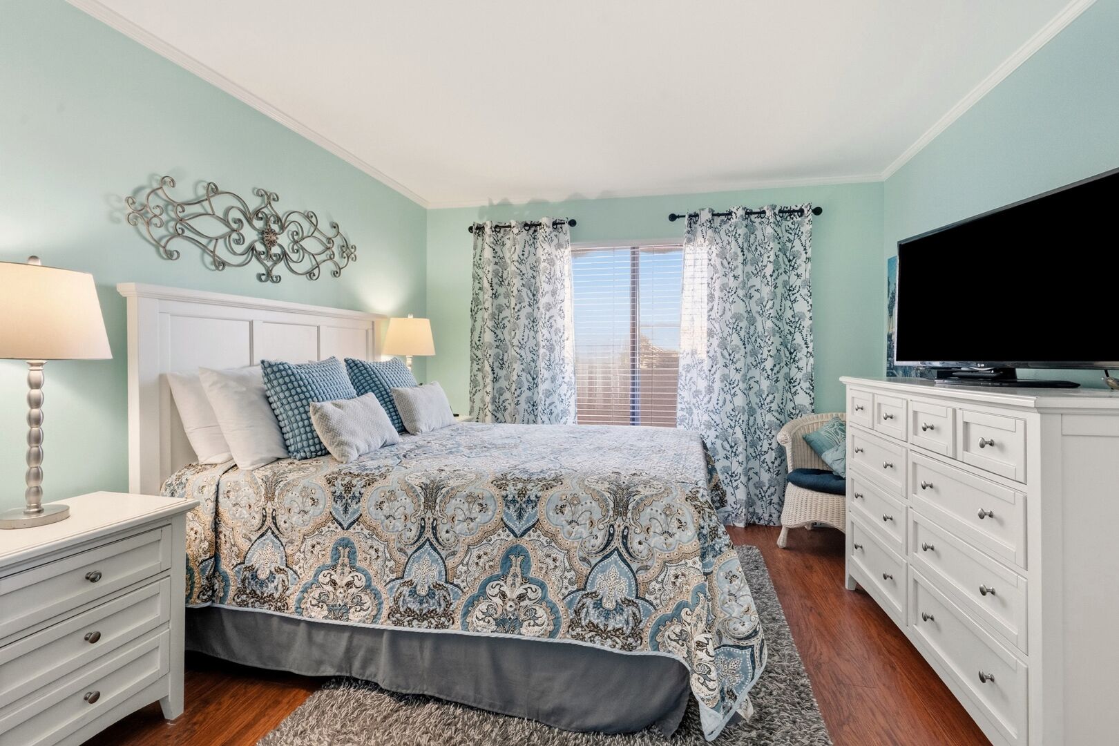 Une chambre à coucher comprenant un lit, des tables de chevet, une commode, un téléviseur et une fenêtre avec des rideaux.