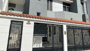 Un edificio moderno con fachada blanca, techo de tejas rojas y puertas de hierro decorativas negras.