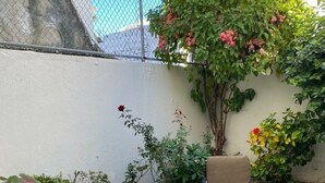 Un patio con mesa y dos sillas, rodeado de plantas diversas y una valla.