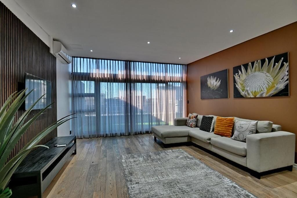 Una sala de estar moderna con un sofá modular, un televisor de pantalla plana y ventanas amplias con cortinas translúcidas.