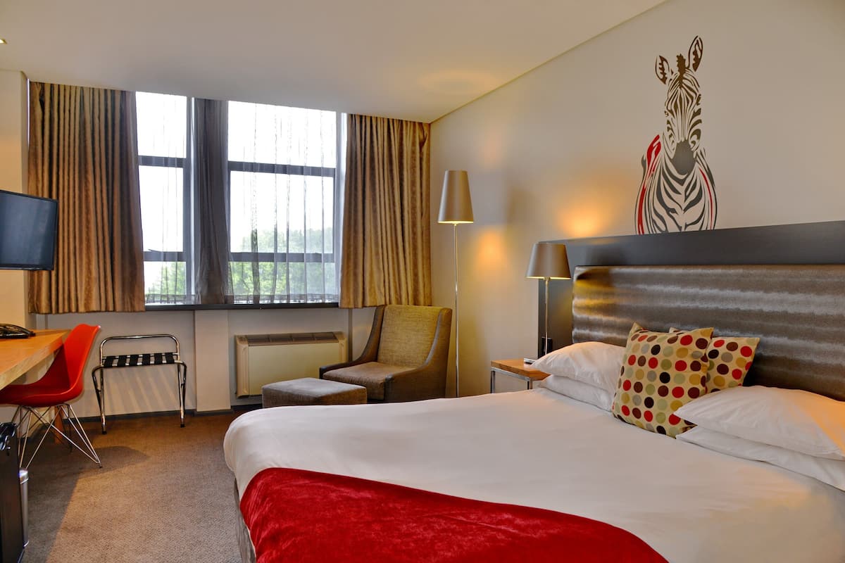 A hotel room with a large bed, a desk with a chair, a radiator, and a wall with a zebra mural.