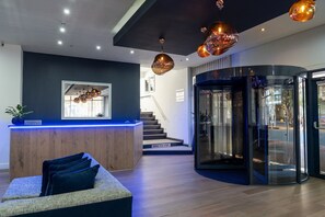 Een moderne receptie met een houten balie, een verlichte counter in blauw en een trap naar een verdieping.