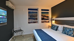 Een hotelkamer met een bed, een aan de muur bevestigde televisie en twee inlijste foto’s van een kustlandschap.
