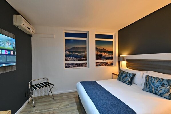 Een hotelkamer met een bed, een aan de muur bevestigde televisie en twee inlijste foto’s van een kustlandschap.