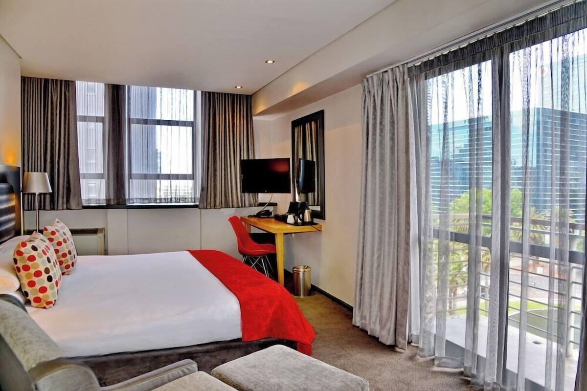 A hotel room with a large bed, a desk, a TV, and a view of the city.
