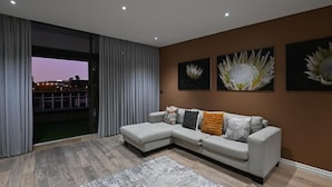 Een moderne woonkamer met een hoekbank, een groot raam met gordijnen, en drie bloemschilderijen aan de muur.