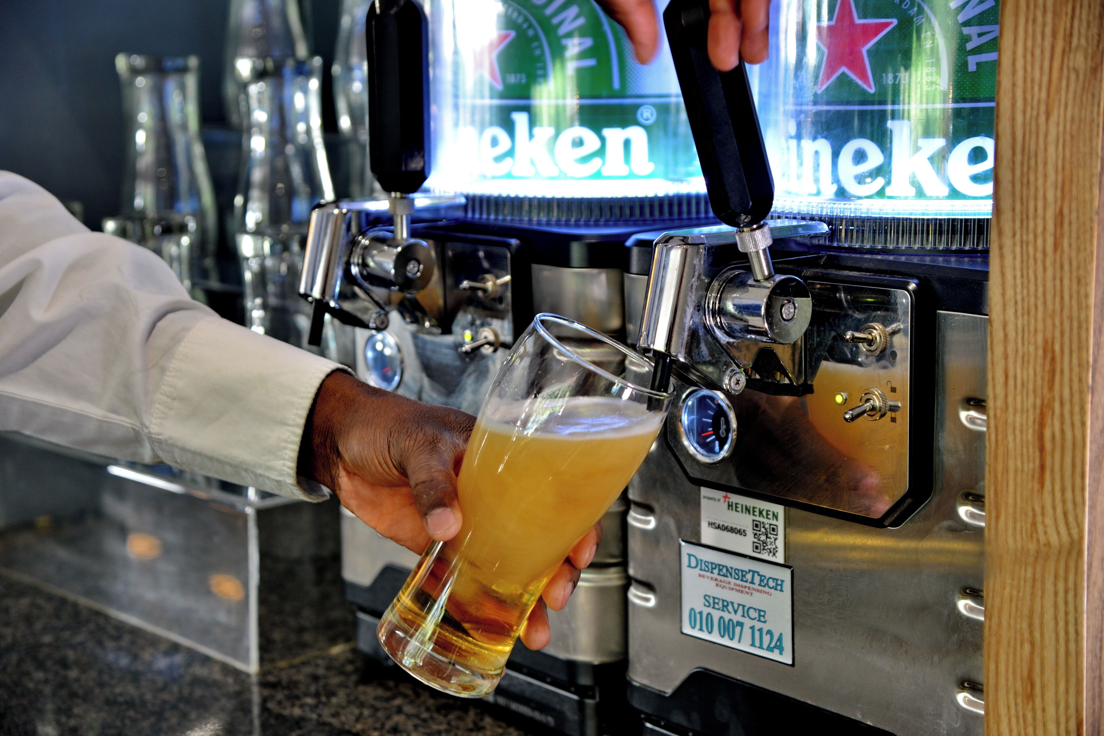 A person pouring beer from a tap labeled "Heineken" into a glass.