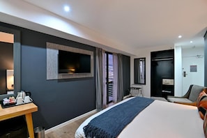 A modern hotel room with a large bed, a desk with coffee-making equipment, a TV, and a view of the outside.