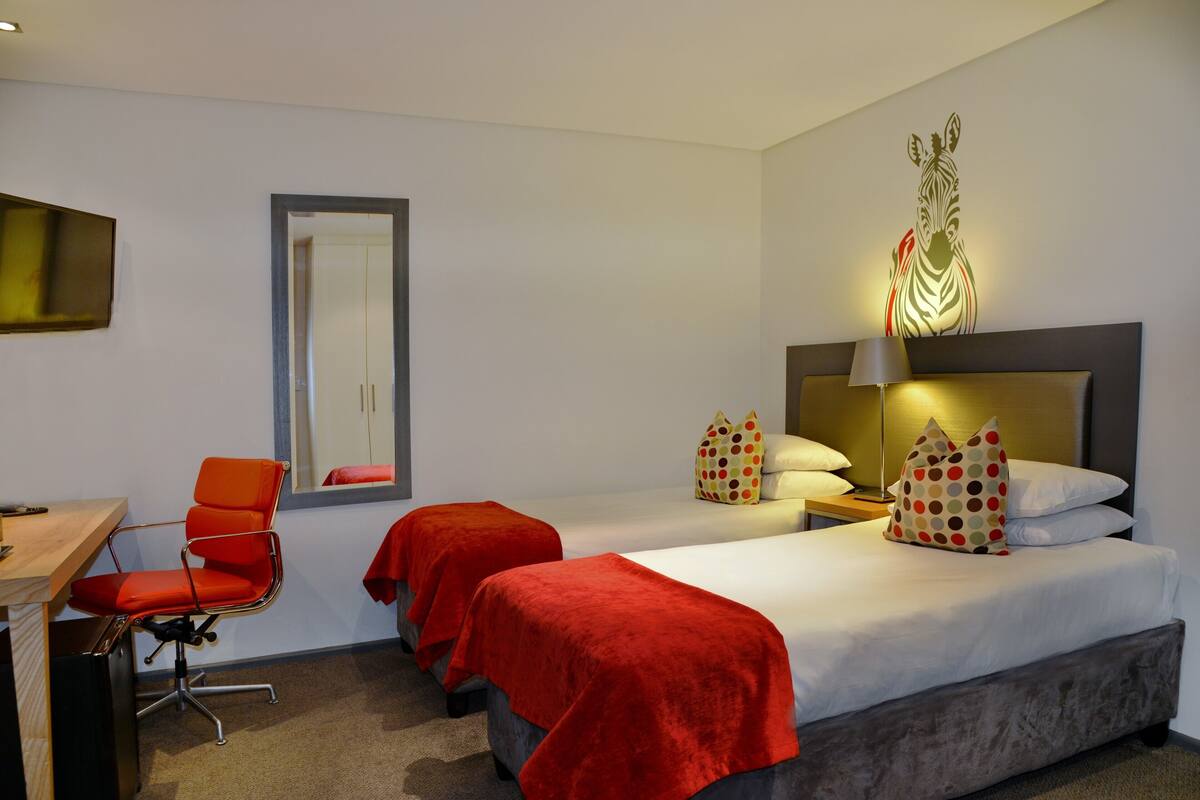 A hotel room with two beds, a desk, and a chair.