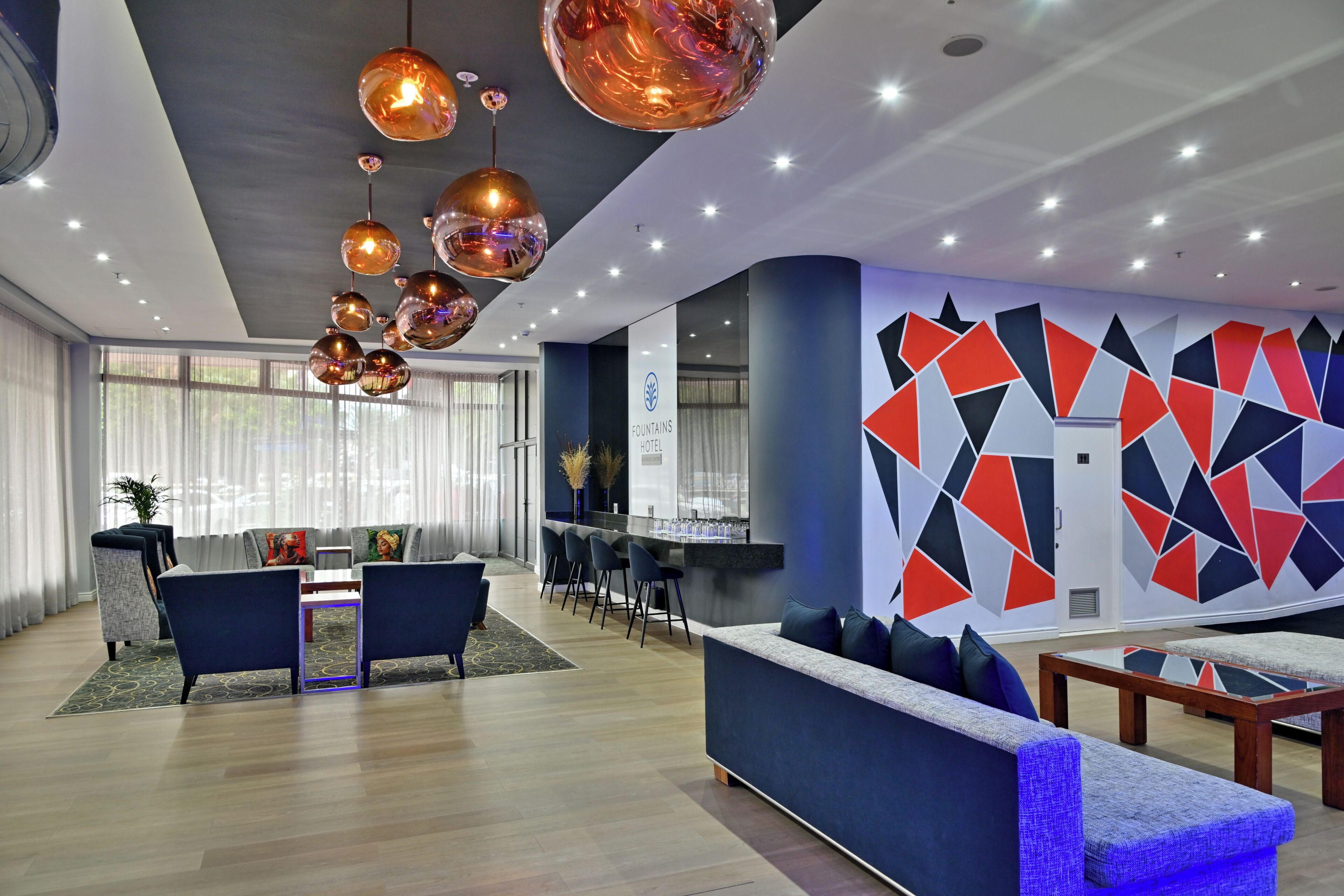 Un moderno vestíbulo de hotel con una zona de estar, una recepción y un diseño geométrico en la pared.
