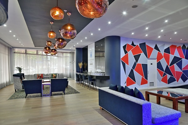 A modern hotel lobby with a seating area, a reception desk, and a geometric wall design.