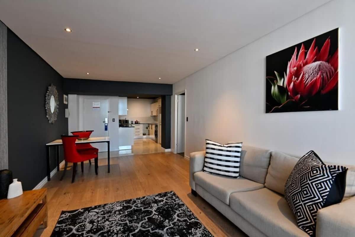 A modern living room with a sofa, a patterned rug, and a painting of a flower.