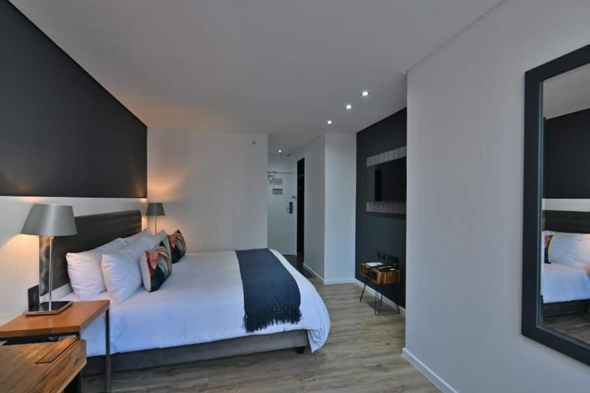 A modern hotel room with a large bed, bedside tables, a mirror, and a view of the hallway.