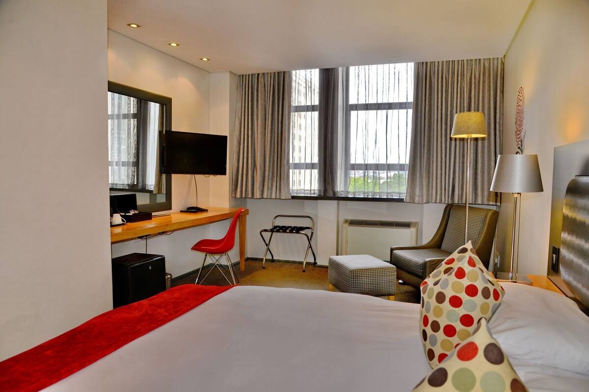 A hotel room with a bed, desk, chair, and a window with curtains.