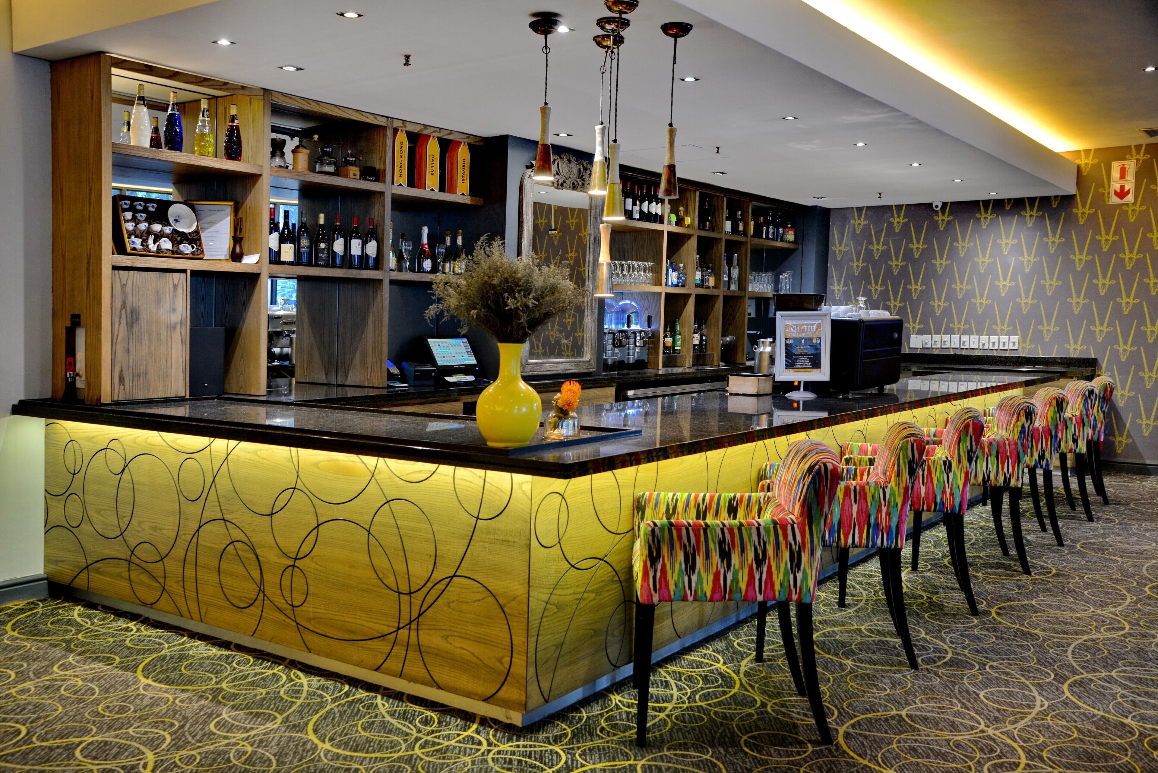 A bar area with a long counter, multiple shelves with bottles, and a patterned carpet.