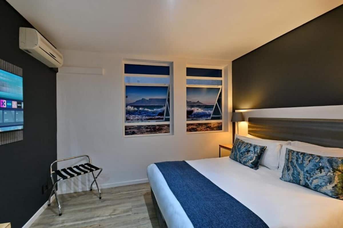 A bedroom with a bed, a nightstand, a wall-mounted air conditioner, and a window with a view of a bridge and mountains.