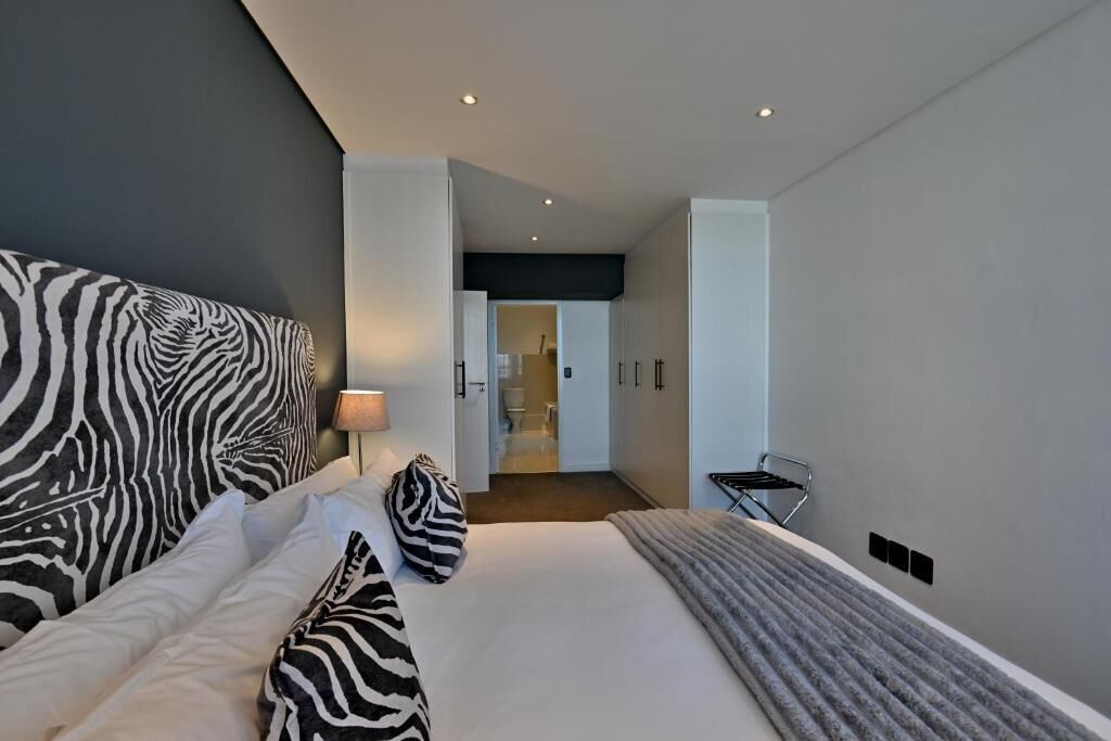 Habitación de hotel moderna con una cama grande, cabecero estampado con motivos de cebra, mesita de noche con lámpara y vistas al baño.