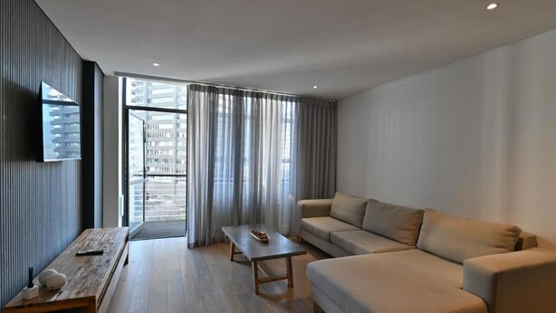 Een moderne woonkamer met een bank, een salontafel en een aan de muur bevestigde televisie.