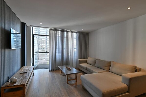 A modern living room with a sofa, a coffee table, and a TV mounted on the wall. - Fountains Hotel by Neighbourgood (Cape Town)
