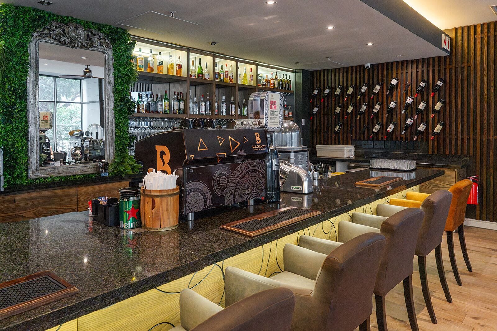 Uma área de bar com balcão, banquetas, máquina de café e adega.
