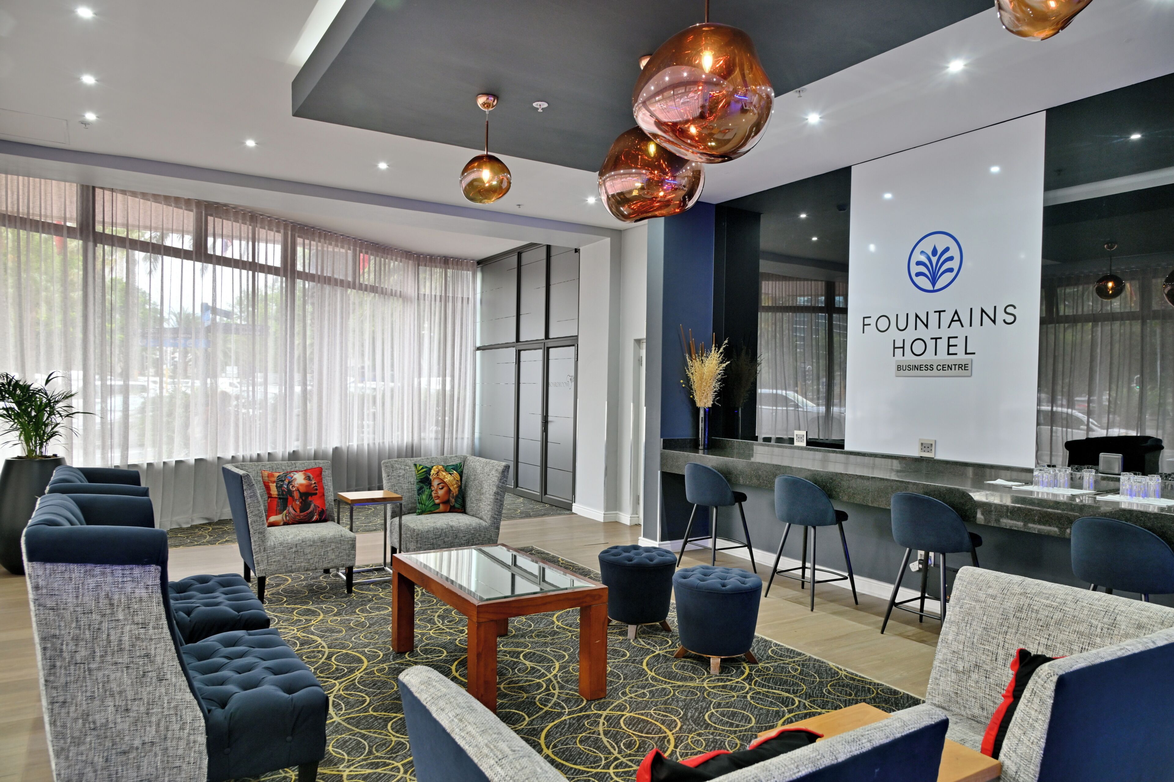 En hotellobby med soffor, ett soffbord, en receptionsdisk och ett stort fönster med gardiner.