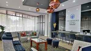 Een hotellobby met banken, een bijzettafeltje, een receptiebalie en een groot raam met gordijnen.