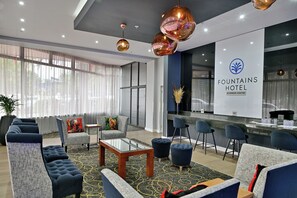 Un hall d’hôtel avec des canapés, une table basse, un comptoir d’accueil et une grande fenêtre avec des rideaux.
