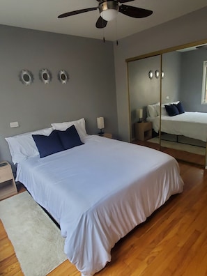 Une chambre avec un grand lit, un ventilateur de plafond, un miroir et une table de chevet.