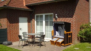 Una casa de ladrillo con un patio, una mesa con cuatro sillas, una silla exterior a rayas y una puerta blanca.