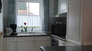 Una cocina con gabinetes blancos, encimera negra, un lavamanos y una ventana con cortinas.