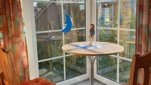 Una habitación con un ventanal grande, una mesa redonda, dos sillas de madera y una pequeña decoración con forma de lechuza.