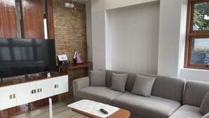 Una sala de estar moderna con un televisor de pantalla plana grande, un mueble de madera, un sofá gris y una mesita de madera con un control remoto.
