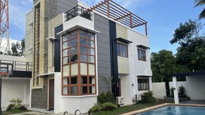 Una casa moderna de dos pisos con piscina, un balcón y vistas a la vegetación circundante.