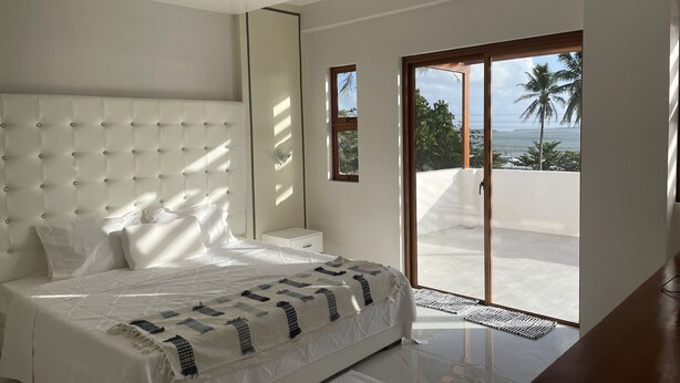 Un dormitorio moderno con una cama grande, una mesita de noche y vistas al exterior a través de una puerta corrediza de vidrio.