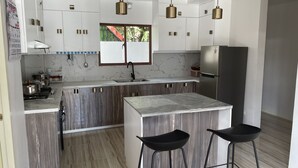 Una cocina moderna con una isla central, electrodomésticos de acero inoxidable y ventana con vistas a la vegetación.