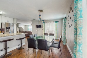 Enjoy meals at the central dining table surrounded by comfortable chairs, with a flat-screen TV above and a large window nearby.